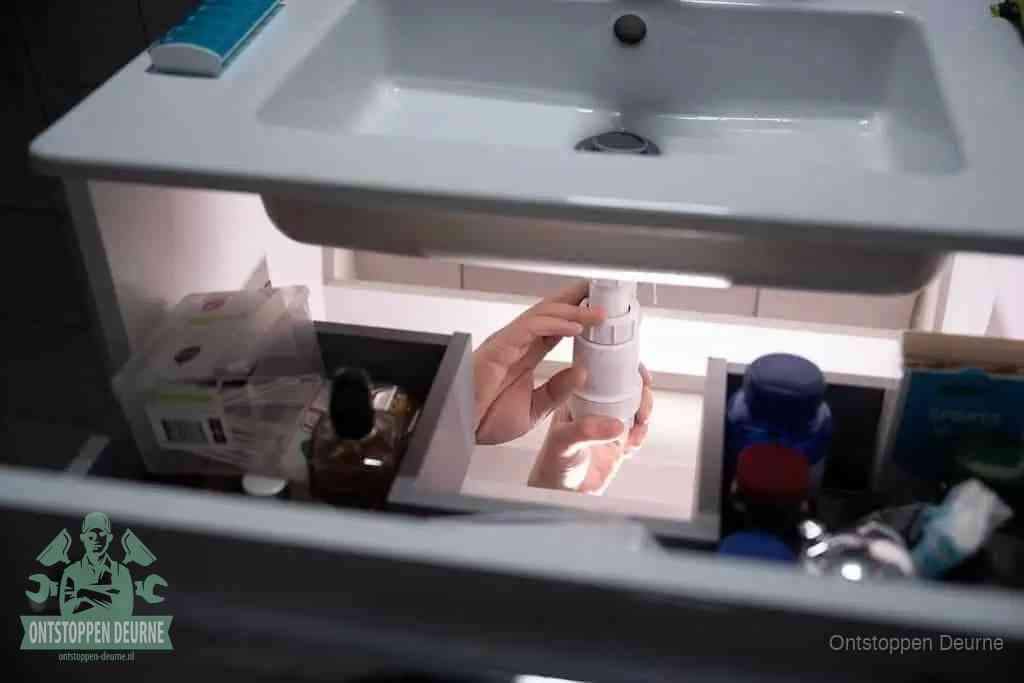 Een pompfles met zeep boven een wastafel, de heet water en afwasmiddel-methode om een vetprop in de afvoer los te maken in Deurne