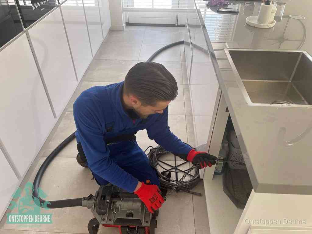 Een monteur ontstopt de keukenafvoer onder de spoelbak met een elektrische veermachine in Deurne