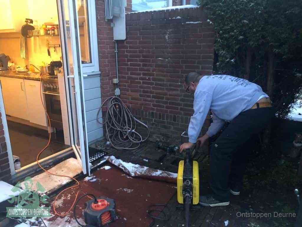 Een monteur werkt buiten bij een open riool-/grondput met een elektrische ontstoppingsmachine om een verborgen afvoerprobleem op te sporen in Deurne