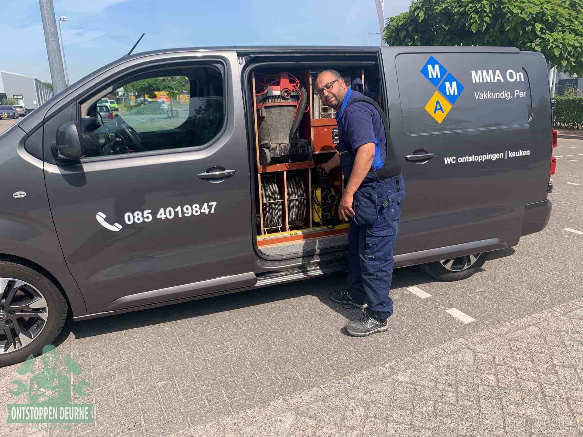 Een monteur bij de open schuifdeur van zijn bedrijfsbus op een parkeerplaats, klaar om de oorzaak van terugkerende afvoerverstoppingen aan te pakken in Deurne