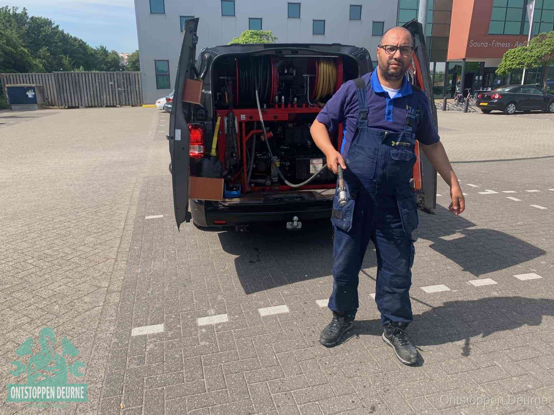Een monteur bij zijn bestelbus met een hogedruk- en rioolreinigingsunit, klaar om de oorzaak van terugkerende wc-verstoppingen aan te pakken in Deurne