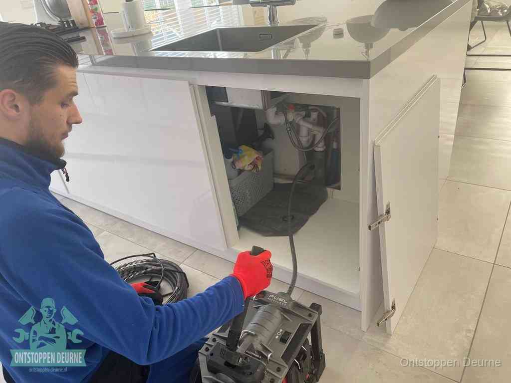 Monteur ontstopt met een veermachine een verstopte afvoer onder de gootsteen in Deurne