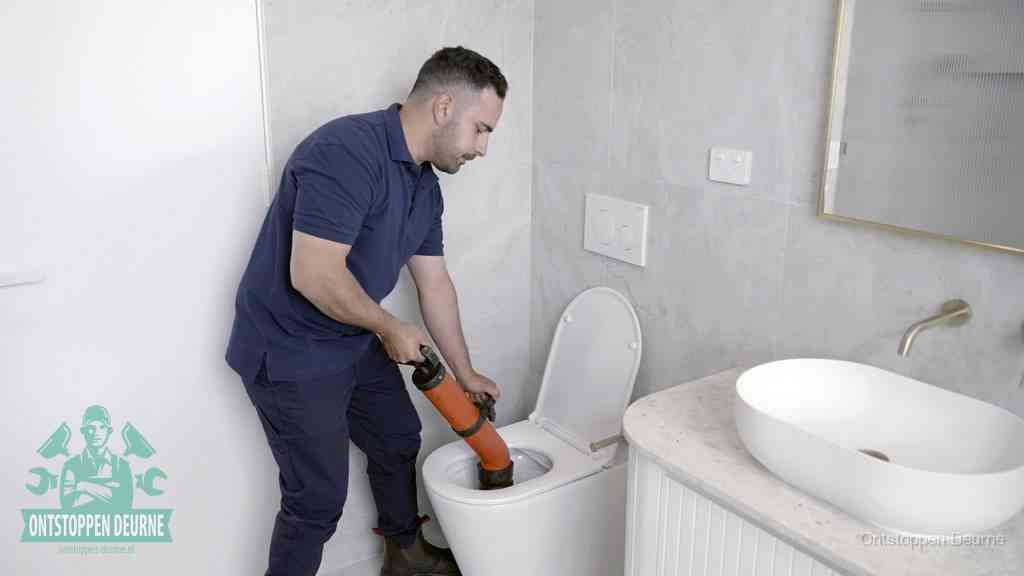 Een man gebruikt een handmatige luchtdruk-ontstopper in een modern betegeld toilet om zelf de wc te ontstoppen in Deurne